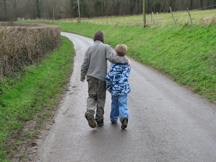 Two boys walking in a country lane in winter. The older boy has his arm around the younger one. 